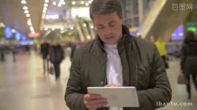 在拥挤的机场大厅里，身穿黑色夹克的年轻人正在用平板电脑上网